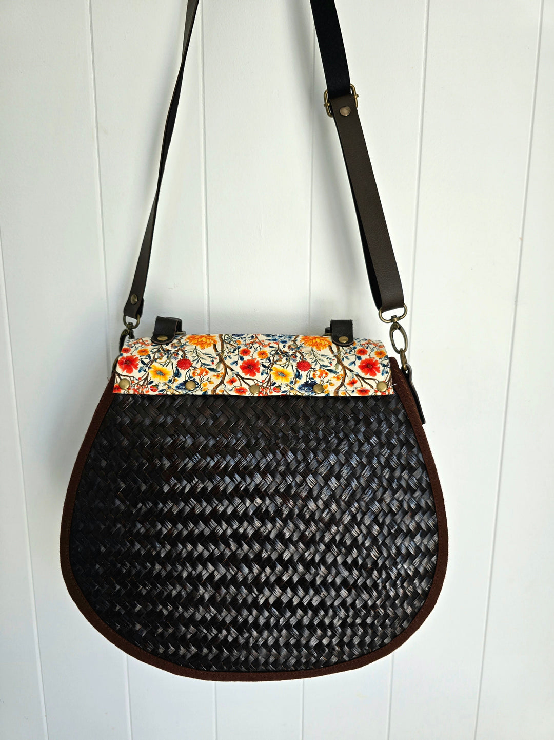 Black woven handbag with floral patterned flap on a white wooden background