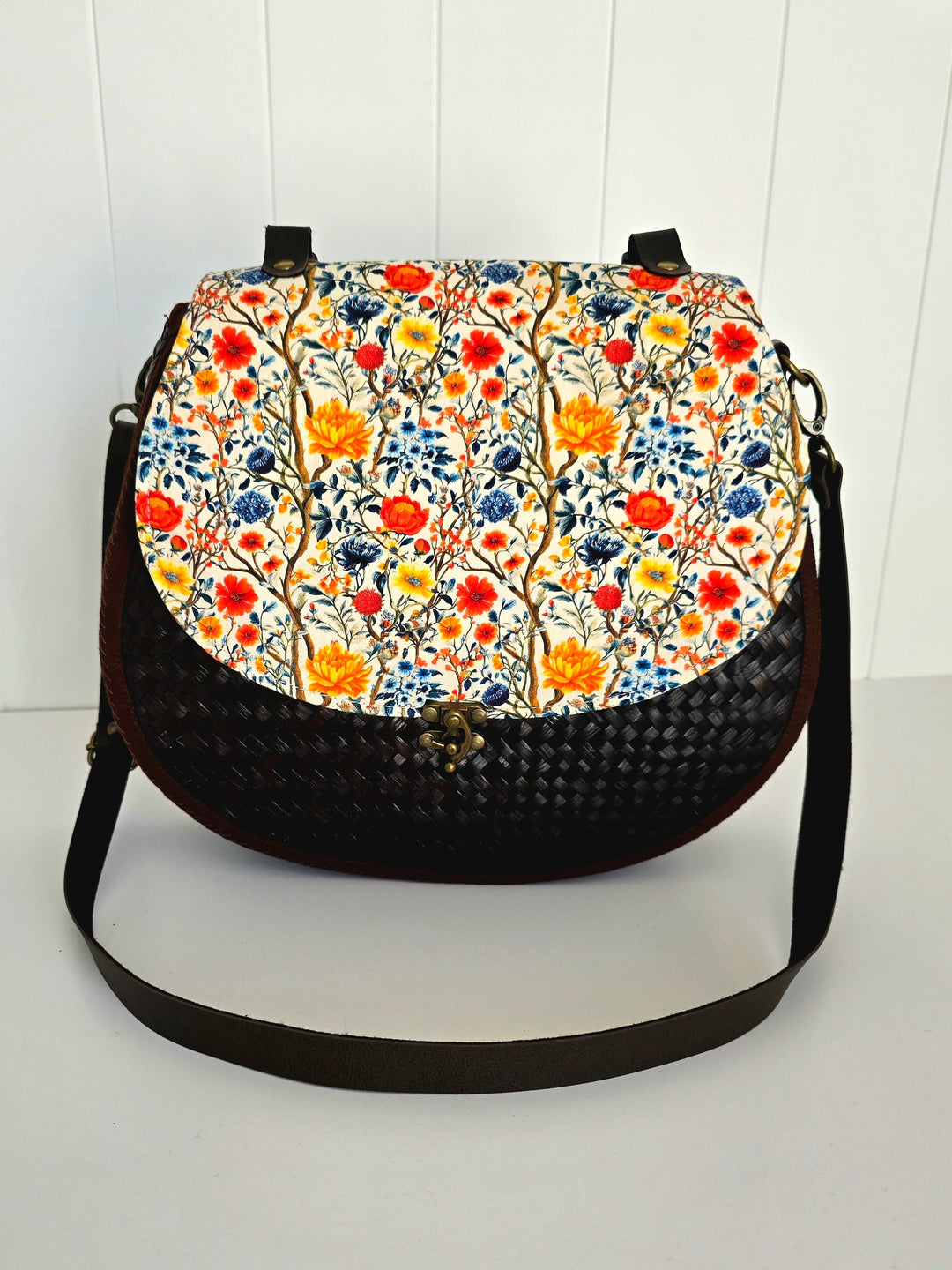Floral patterned handbag with black strap on a white background