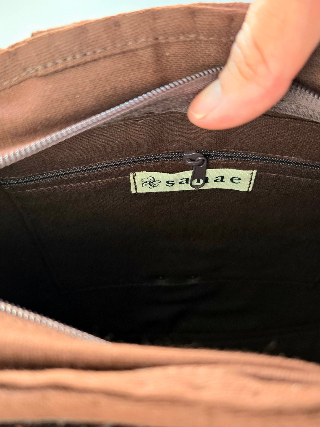 Close-up of a brown bag with a visible brand logo, held by a hand.
