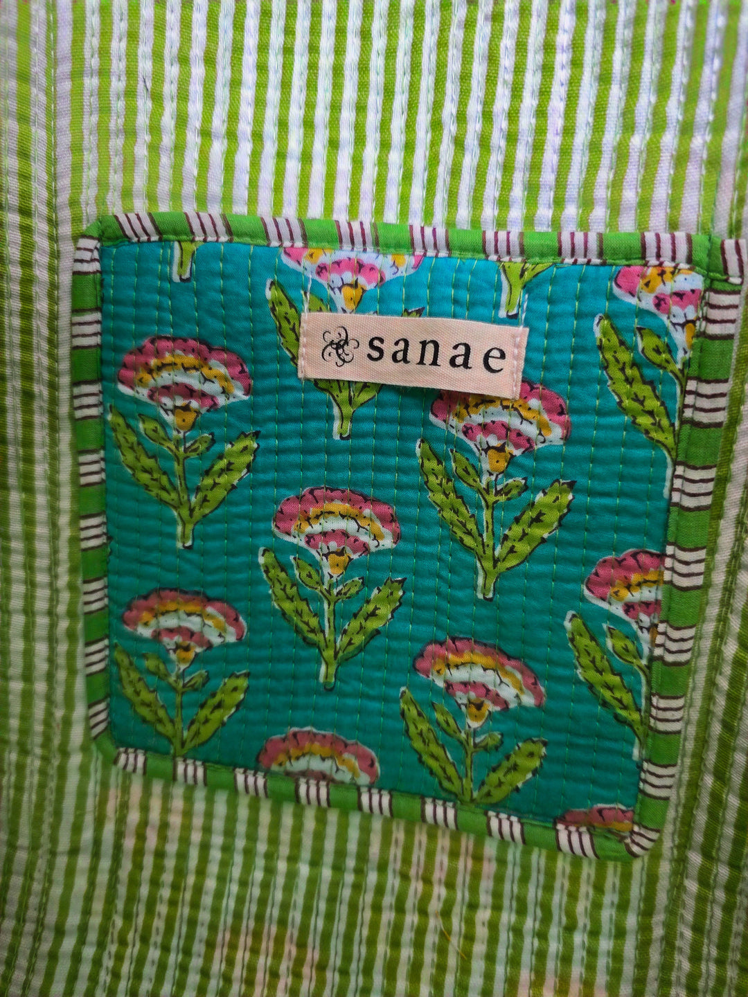 Teal fabric patch with floral patterns and 'sanae' label on a green striped background