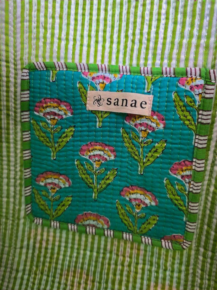 Teal fabric patch with floral patterns and 'sanae' label on a green striped background