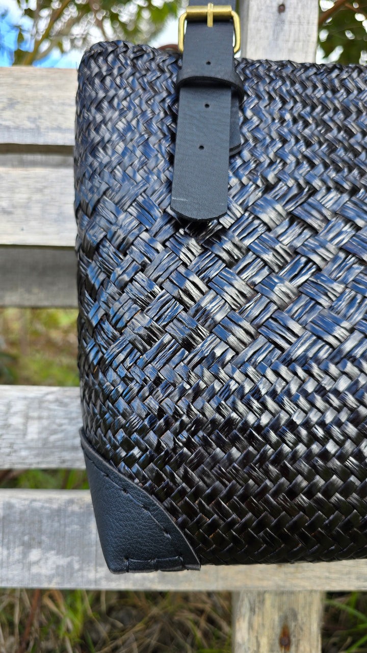 Woven handbag with leather strap on a wooden surface