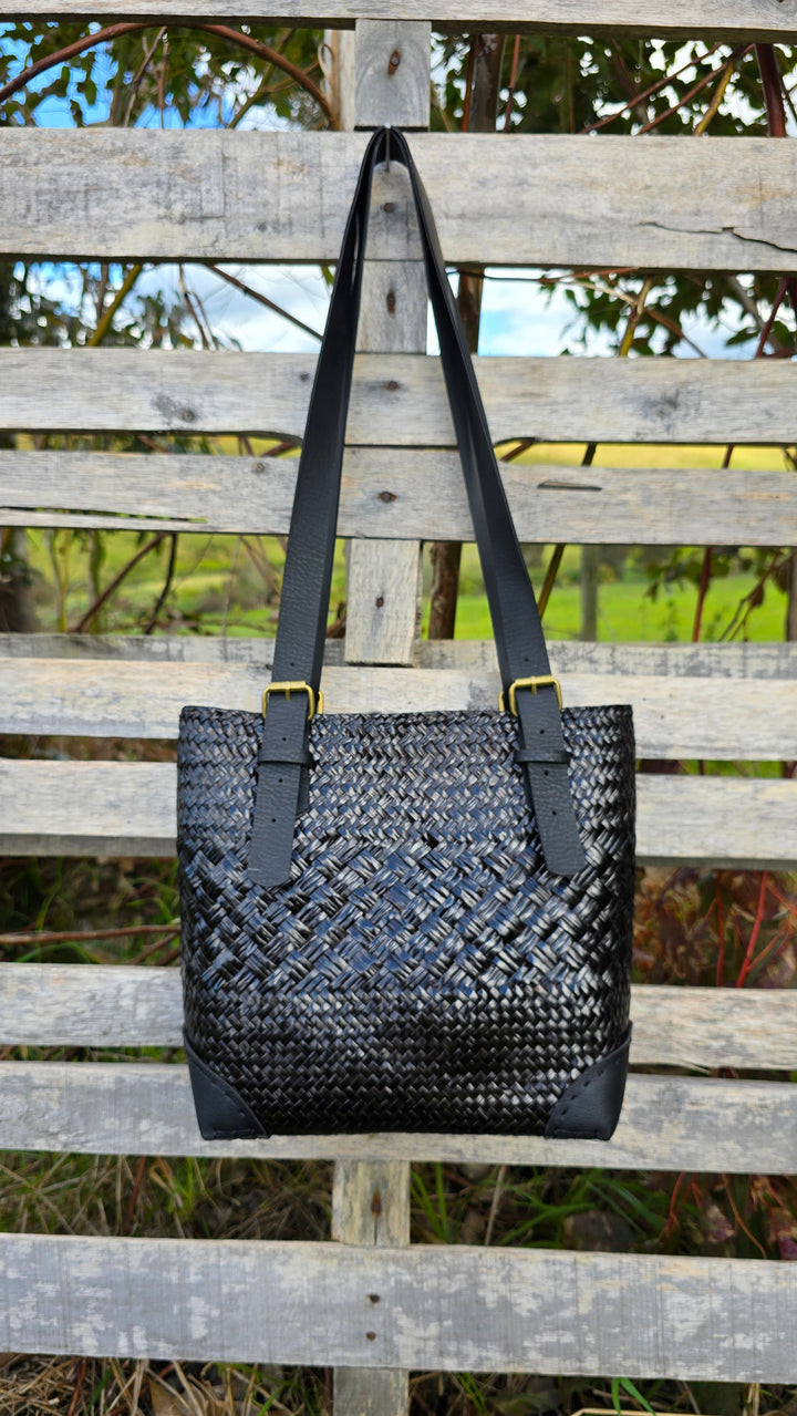 Black woven handbag on a wooden fence with a natural background