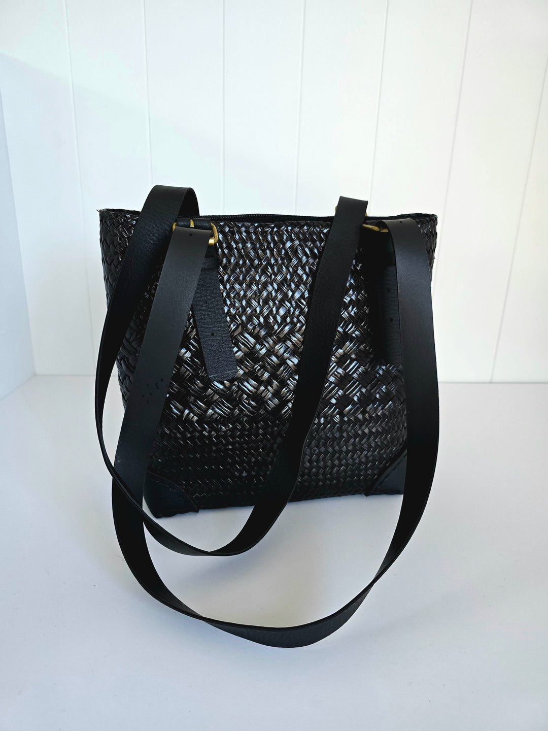 Black woven handbag with a strap on a white background