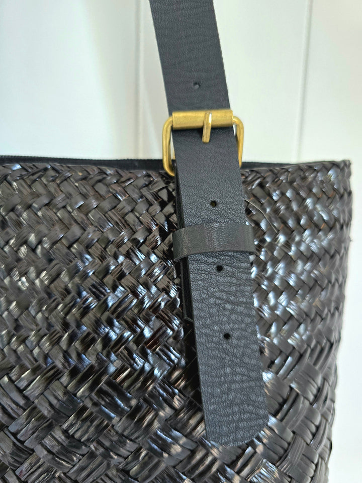 Black woven bag with a black strap and gold buckle on a white background