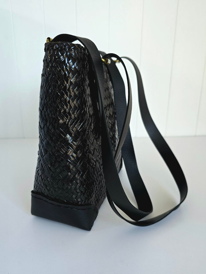 Side of black woven handbag with a strap on a white background