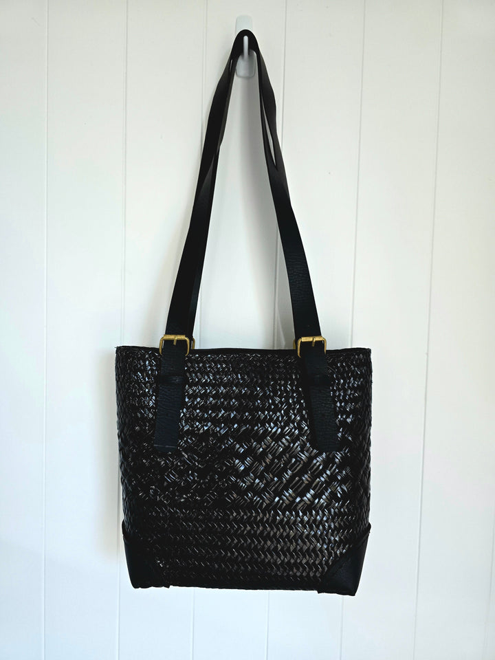 Black woven handbag with black straps on a white wooden background